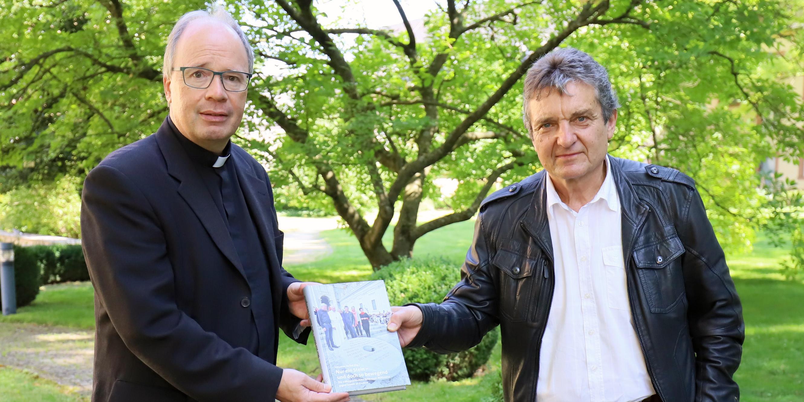 Johannes Heibel (links) übergibt den Bildband zum „Mahnenden Mühlstein“ an Bischof Ackermann. (Foto: Christina Libeaux/Bistum Trier)