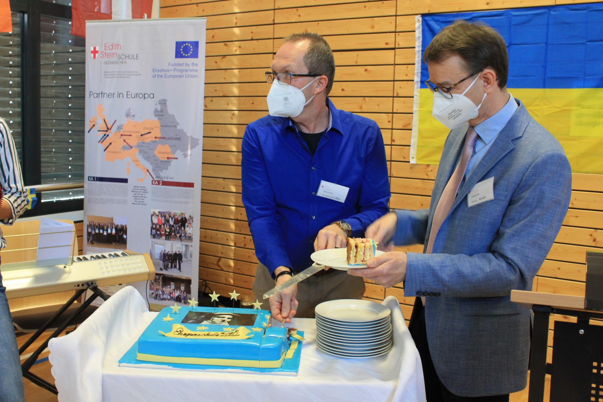 Der stellvertretende Schulleiter Karl Josef Klär und Schulleiter Markus Kirsch schneiden die Torte an - in den ukrainischen Nationalfarben blau-gelb.