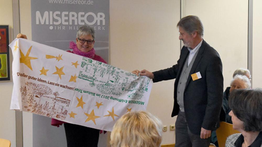 Gaby Thiery aus Saarlouis und Ludwig Kuhn präsentieren den von den Sternsingern der Saarlouiser Pfarreiengemeinschaft Rechts der Saar mitgestalteten Tischläufer aus Burkina Faso