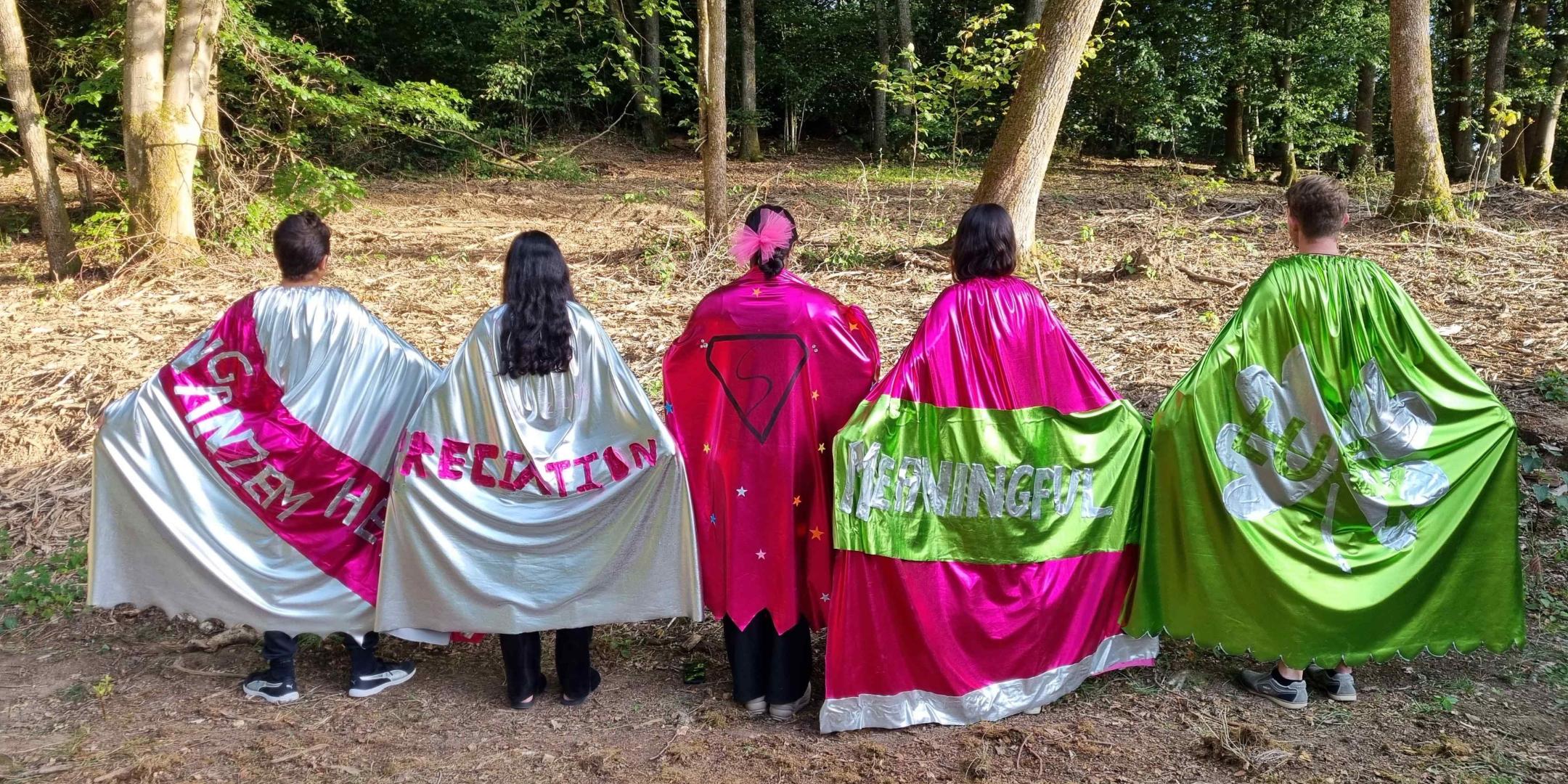 Junge Menschen von hinten mit glitzernden Umhängen.