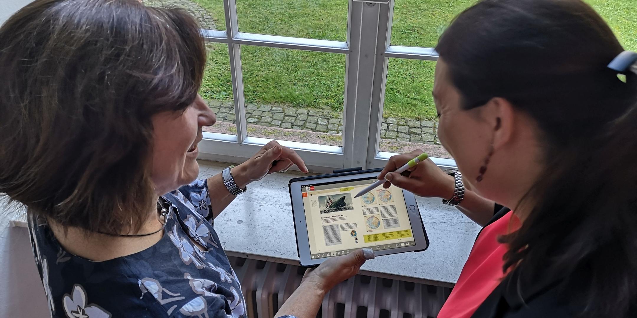 Schulleiterin Johanna Neuhaus (links, Bischöfliche Förderschule St. Josef Trier) und Konrektorin Sandra Klopp (St.-Maximin-Schule Trier) testen ein IPad der sechsten Generation, auf dem ein digitales Lehrwerk geöffnet ist, mit dem man unter anderem Arbeitsblätter öffnen und Tafelbilder darstellen kann.
