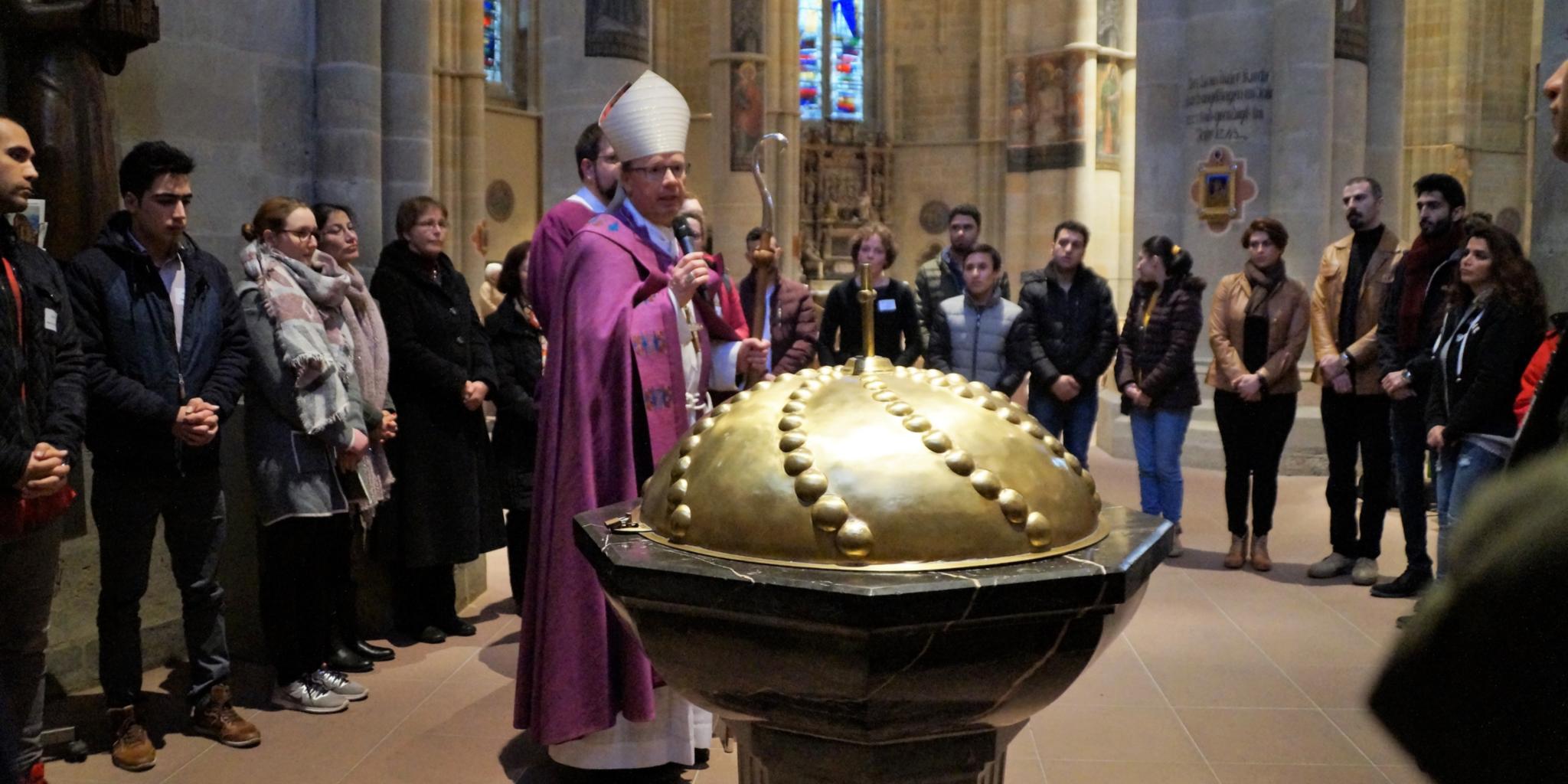 Am Taufbrunnen in der Liebfrauenkirche beginnt für 29 Frauen und Männer die Feier ihrer Zulassung zu den Sakramenten, die Bischof Ackermann erteilt.