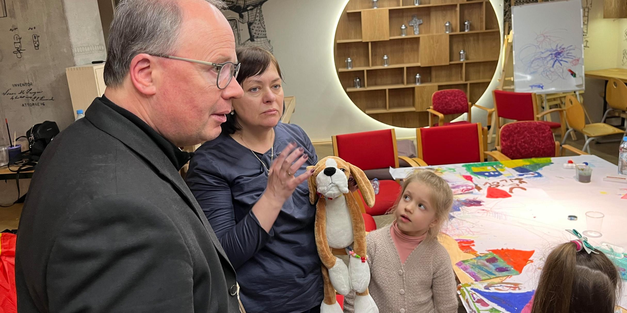 Der Bischof zu Besuch in einem Treffpunkt der Malteser, wo geflüchtete Kinder spielen können. Zu Beginn bekommen sie ein Stofftier überreicht, das sie auch umhängen können und das das Gefühl der Geborgenheit geben soll