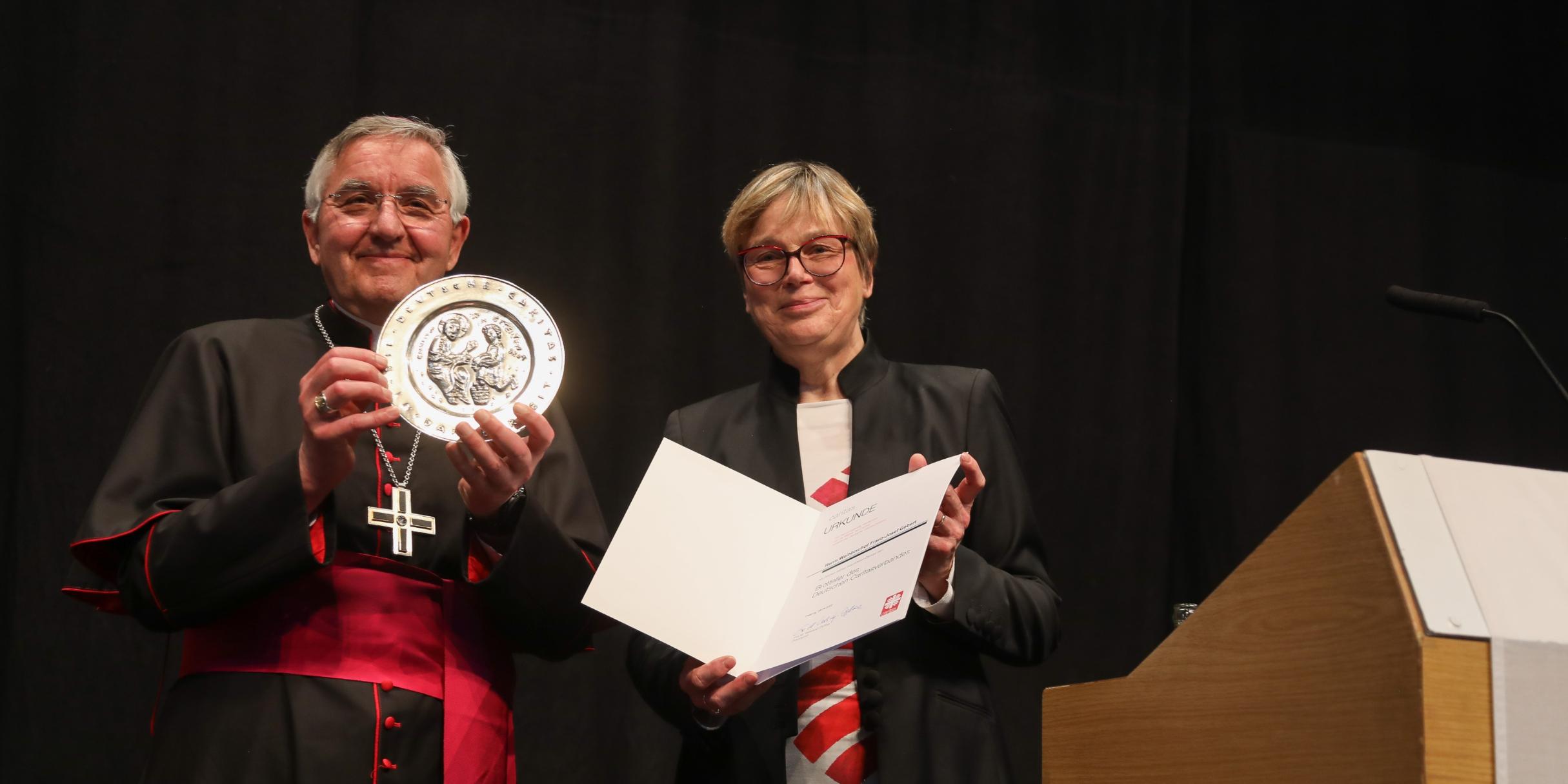 Weihbischof Gebert freut sich über den Brotteller, den ihm Caritas-Präsidentin Eva Maria Welskop-Deffaa überreicht hat. Foto: DiCV Trier/Thewalt