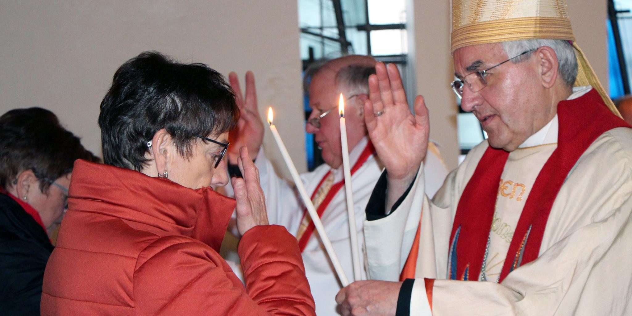 Weihbischof Gebert erteilt einer Christin den Blasiussegen. Er hat eine Kerze in der Hand
