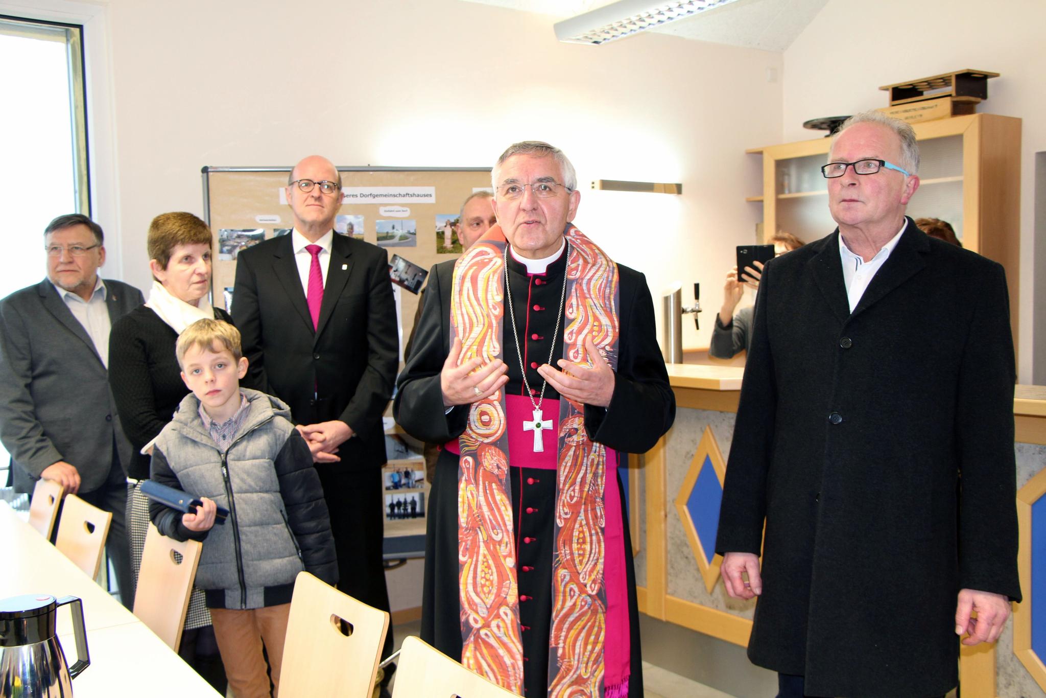 Weihbischof Gebert segnet das neue Dorf- und Feuerwehrhaus ein. Mit ihm auf dem Foto zu sehen sind noch andere Personen, die im Ort wohnen