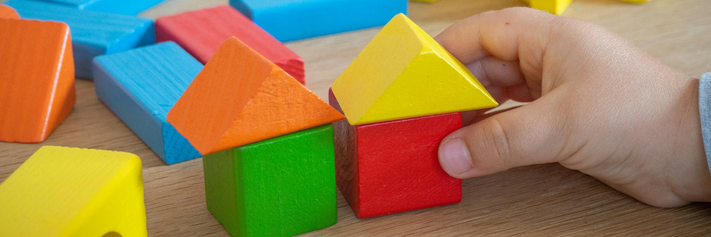 Kinderhand baut mit bunten Holzspielklötzen kleine Häuser.