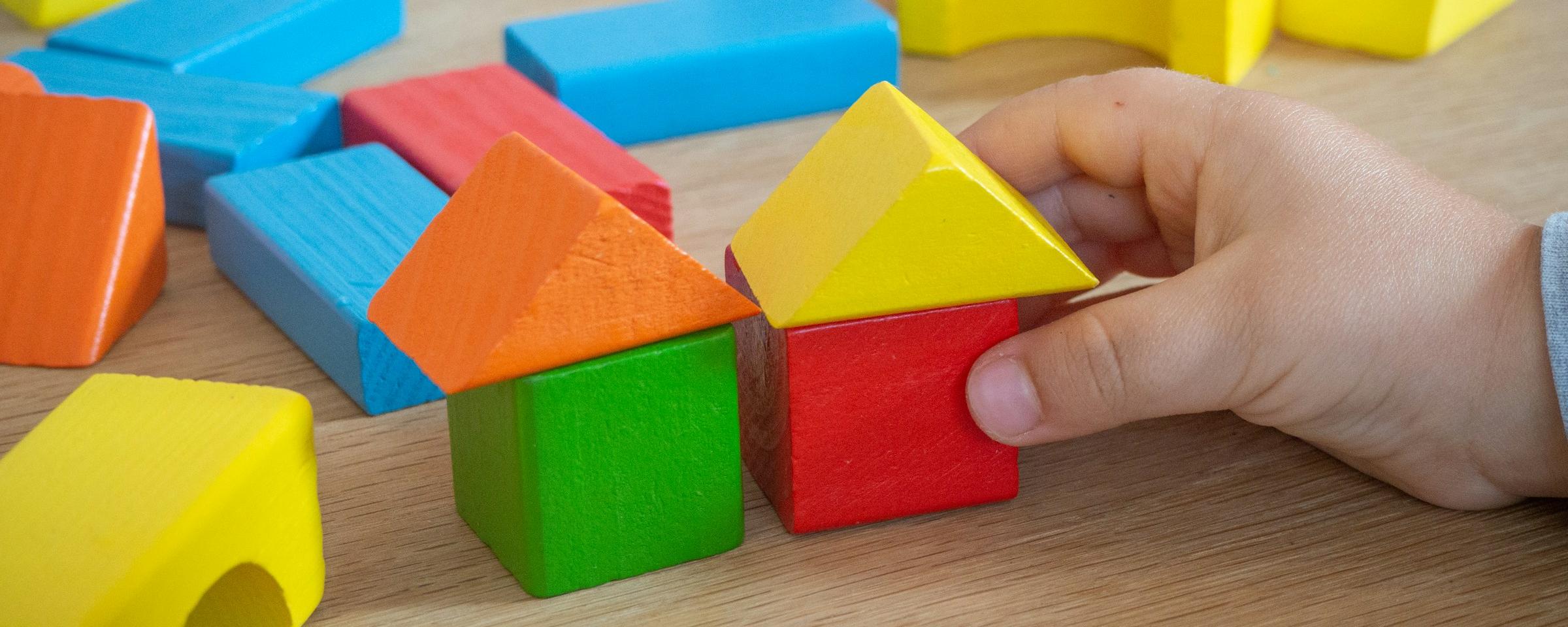 Kinderhand baut mit bunten Holzspielklötzen kleine Häuser.