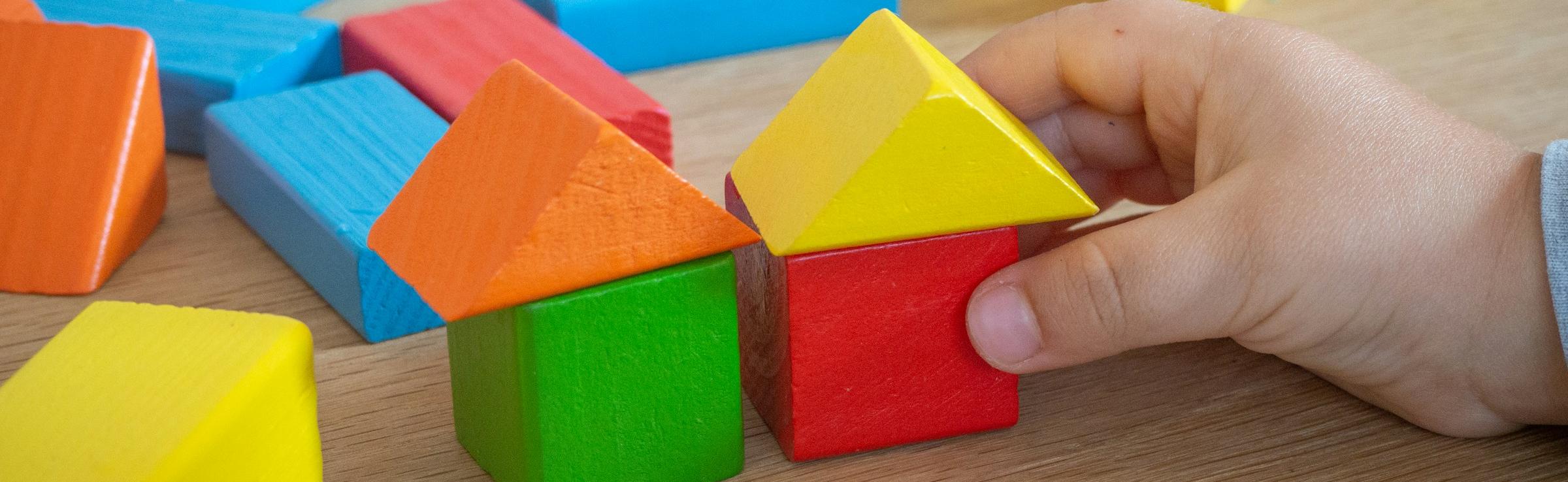 Kinderhand baut mit bunten Holzspielklötzen kleine Häuser.