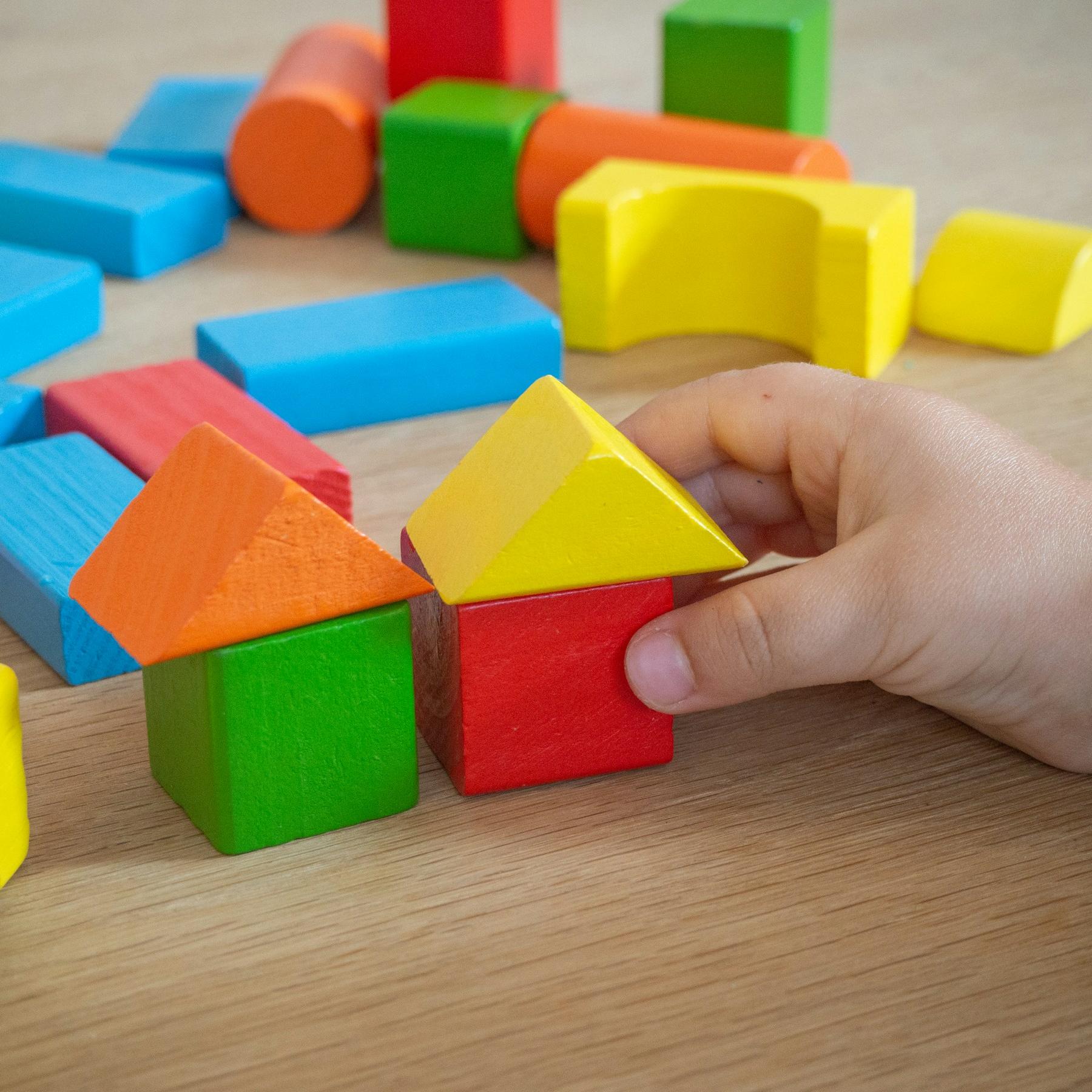 Kinderhand baut mit bunten Holzspielklötzen kleine Häuser.