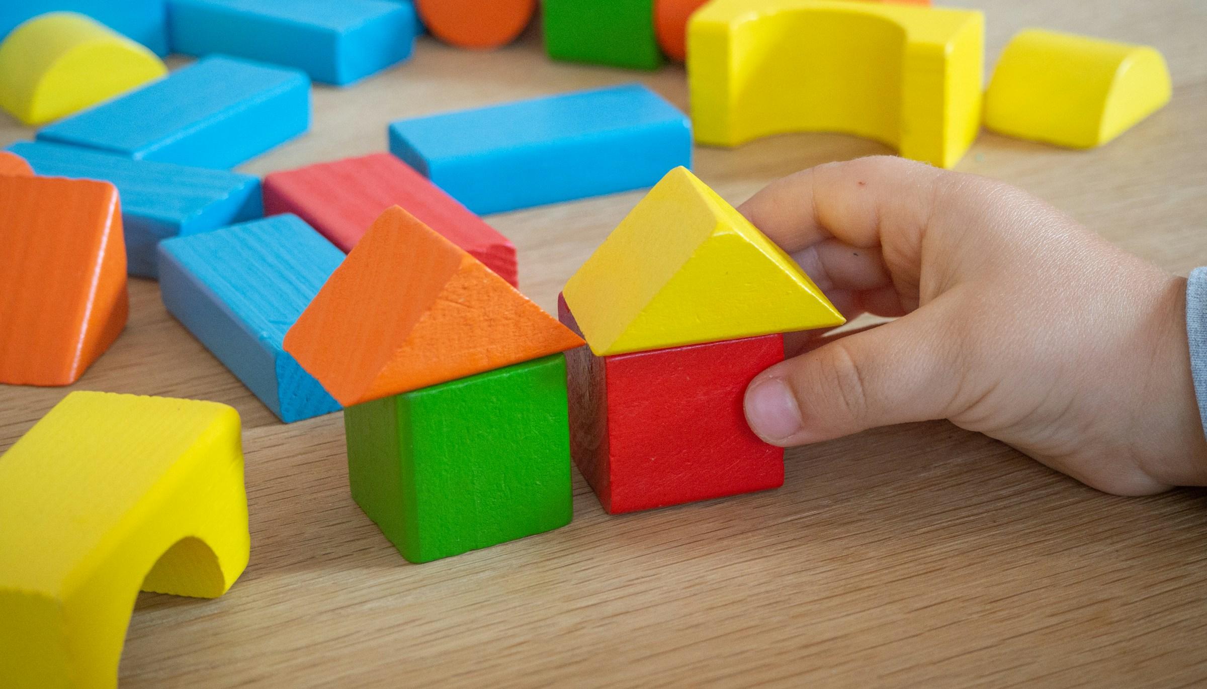 Kinderhand baut mit bunten Holzspielklötzen kleine Häuser.