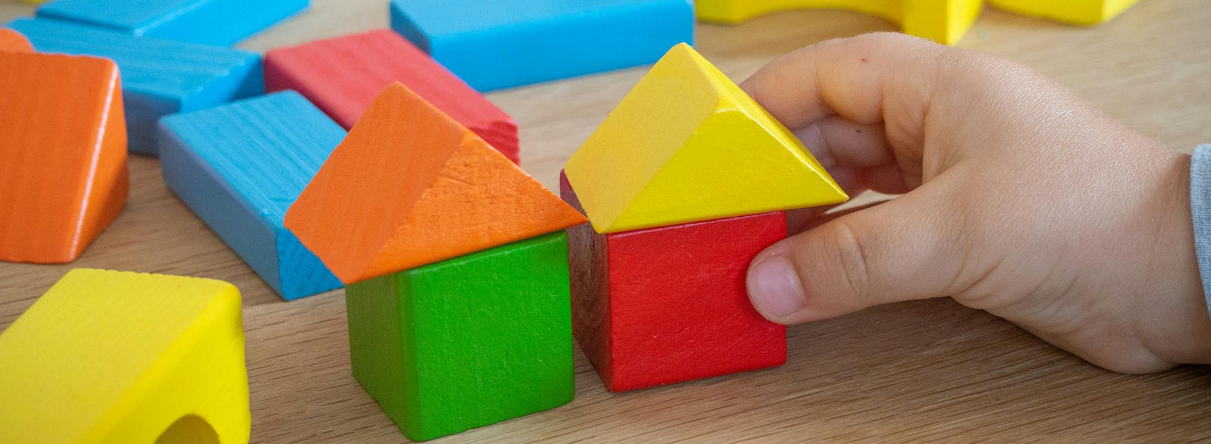 Kinderhand baut mit bunten Holzspielklötzen kleine Häuser.