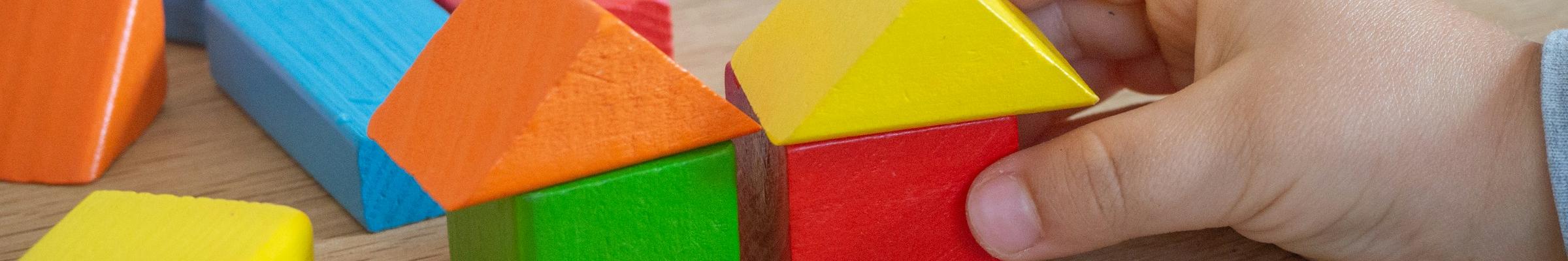 Kinderhand baut mit bunten Holzspielklötzen kleine Häuser.