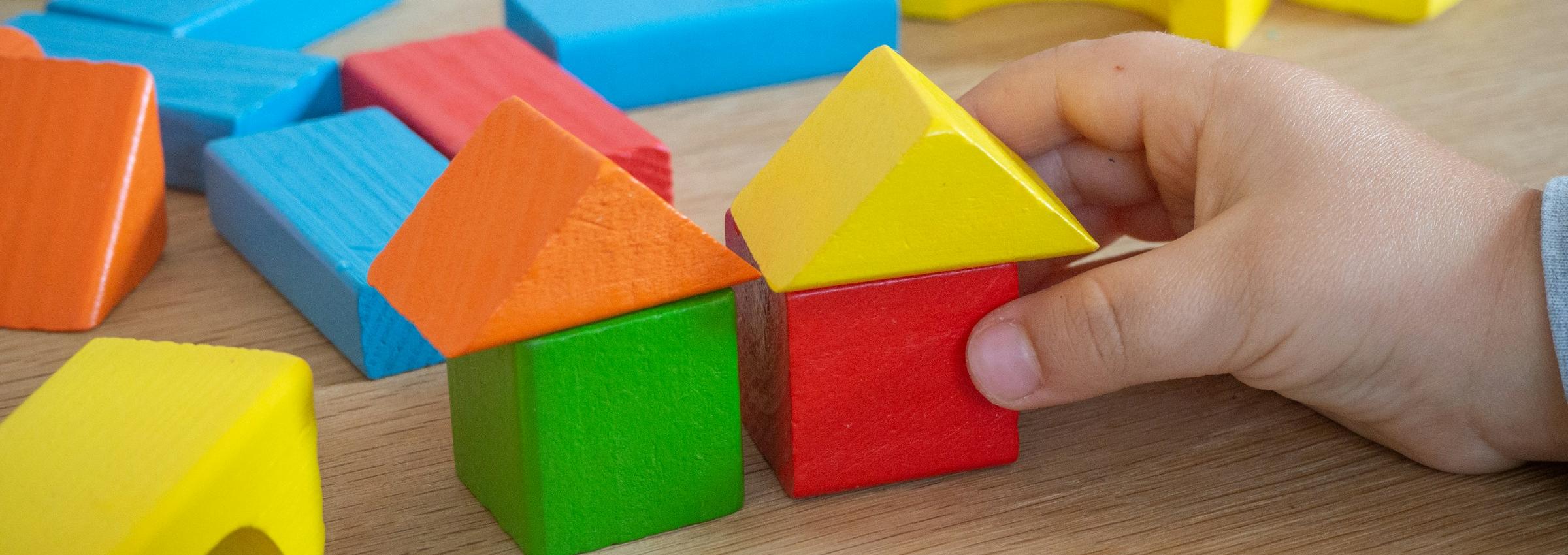 Kinderhand baut mit bunten Holzspielklötzen kleine Häuser.