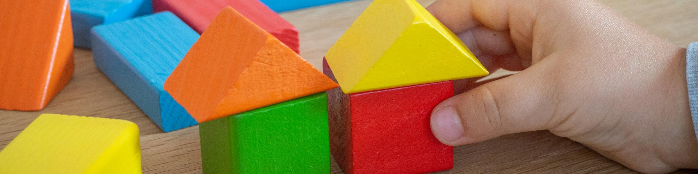 Kinderhand baut mit bunten Holzspielklötzen kleine Häuser.
