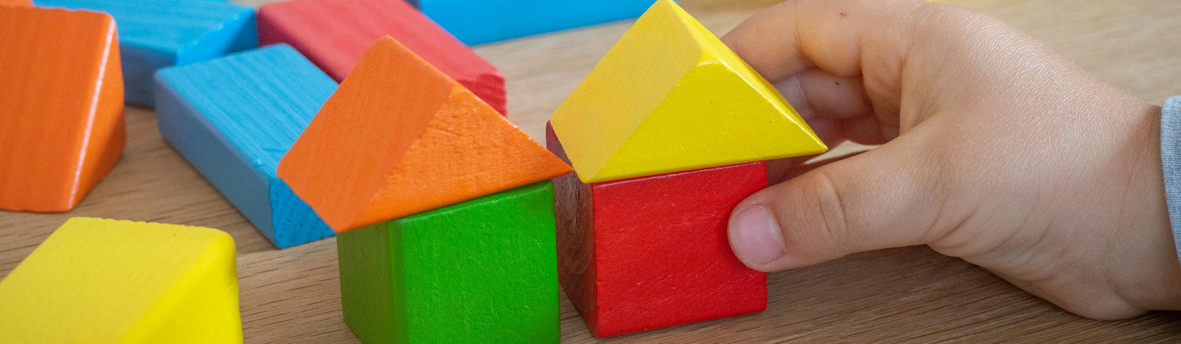 Kinderhand baut mit bunten Holzspielklötzen kleine Häuser.