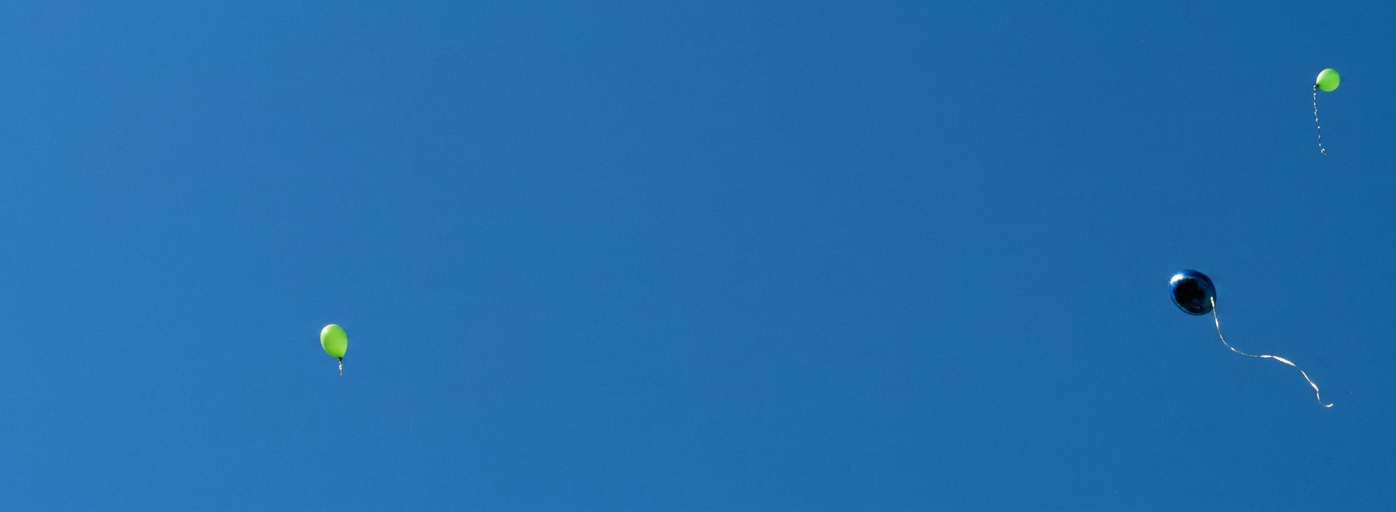 ein blauer und mehrere grüne Luftballons fliegen in den Himmel