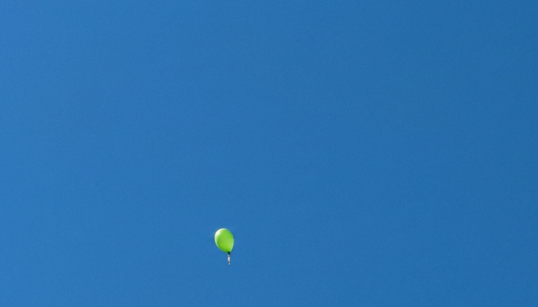 ein blauer und mehrere grüne Luftballons fliegen in den Himmel