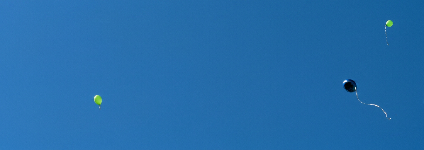 ein blauer und mehrere grüne Luftballons fliegen in den Himmel