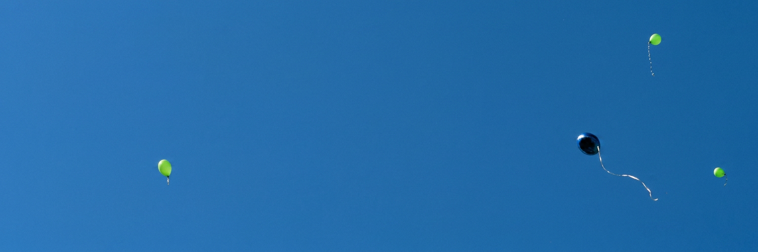 ein blauer und mehrere grüne Luftballons fliegen in den Himmel