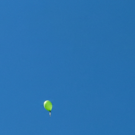 ein blauer und mehrere grüne Luftballons fliegen in den Himmel