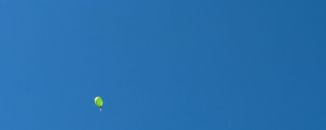 ein blauer und mehrere grüne Luftballons fliegen in den Himmel