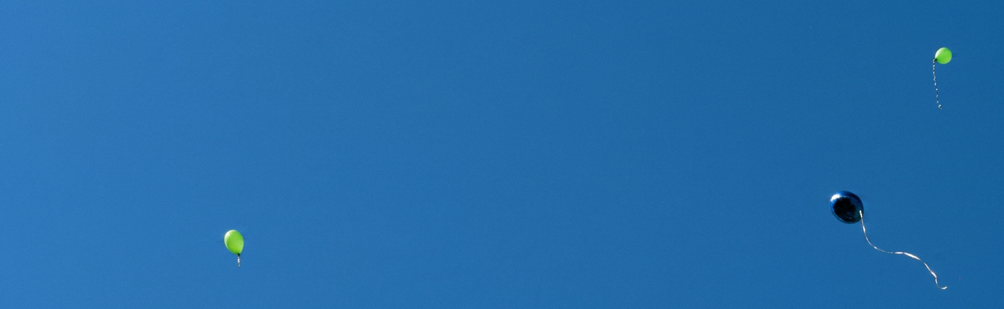 ein blauer und mehrere grüne Luftballons fliegen in den Himmel