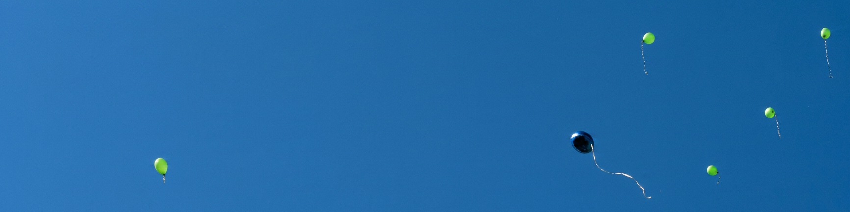 ein blauer und mehrere grüne Luftballons fliegen in den Himmel