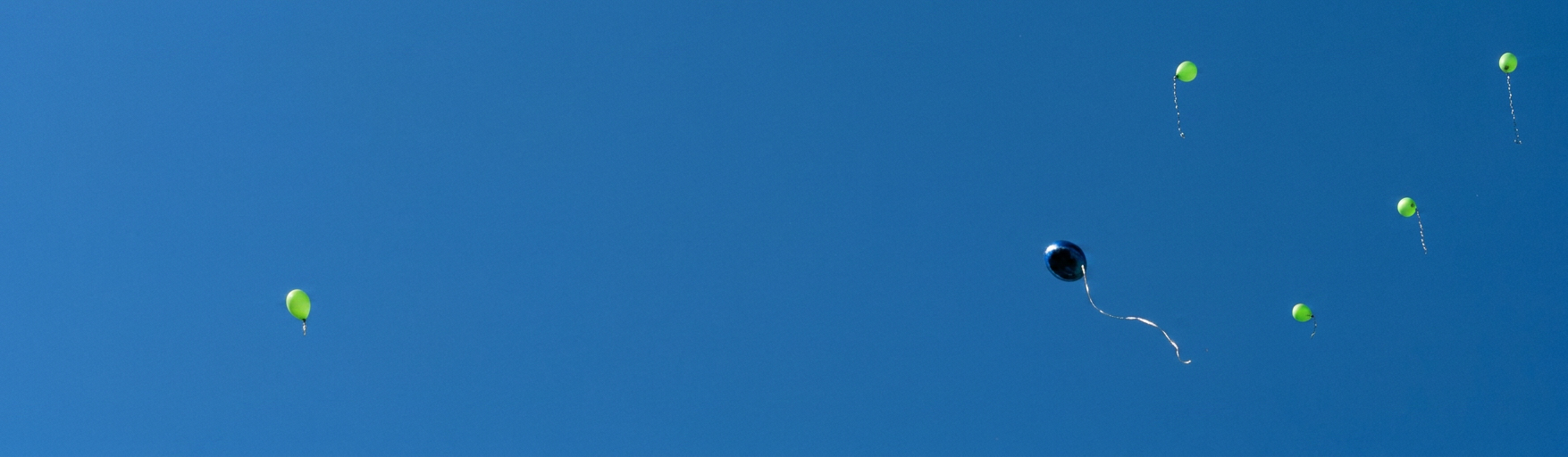 ein blauer und mehrere grüne Luftballons fliegen in den Himmel