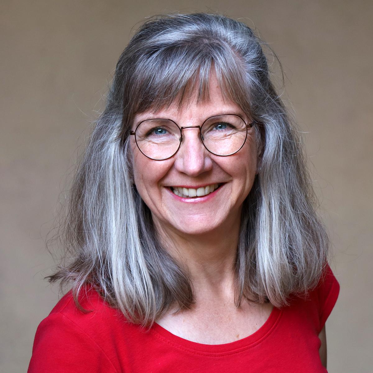 Margit Haubrich Man sieht eine Frau mit Brille und schulterlangen, grauen Haaren, die lächelt.