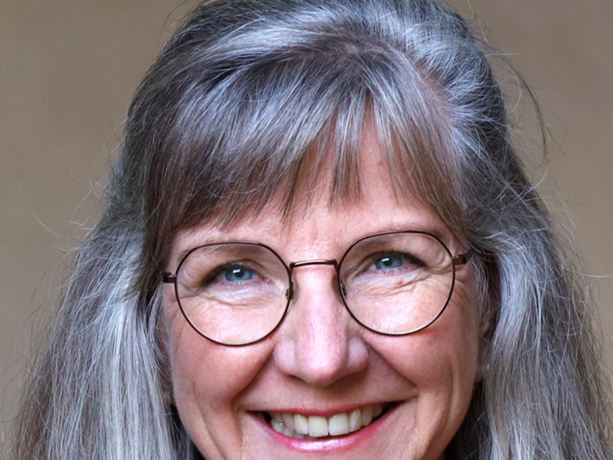 Man sieht eine Frau mit Brille und schulterlangen, grauen Haaren, die lächelt.