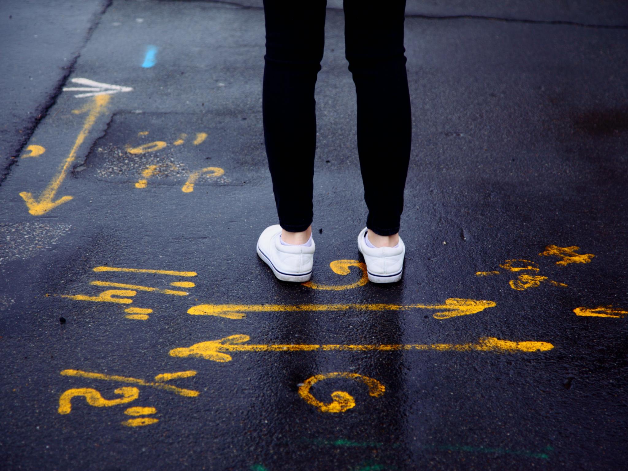 Eine Person steht auf einer Straße, die mit mehreren kryptischen Zeichen und Pfeilen bemalt ist