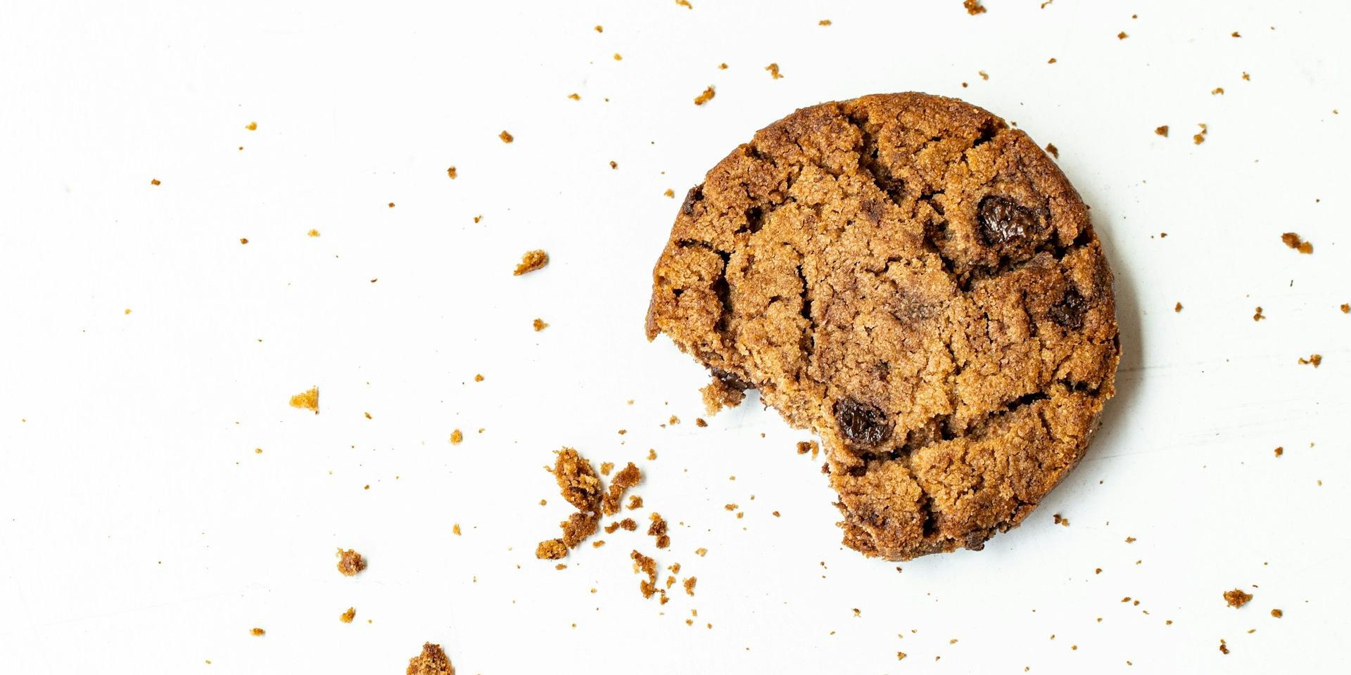 Man sieht einen angebissenen Cookie mit Krümeln auf einer weißen Fläche