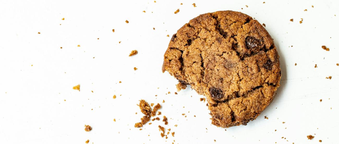 Man sieht einen angebissenen Cookie mit Krümeln auf einer weißen Fläche
