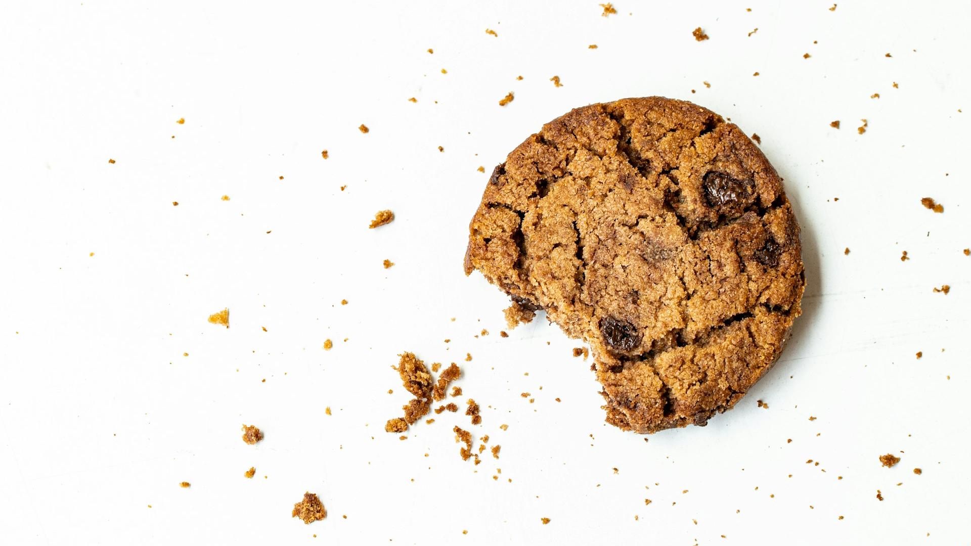Man sieht einen angebissenen Cookie mit Krümeln auf einer weißen Fläche