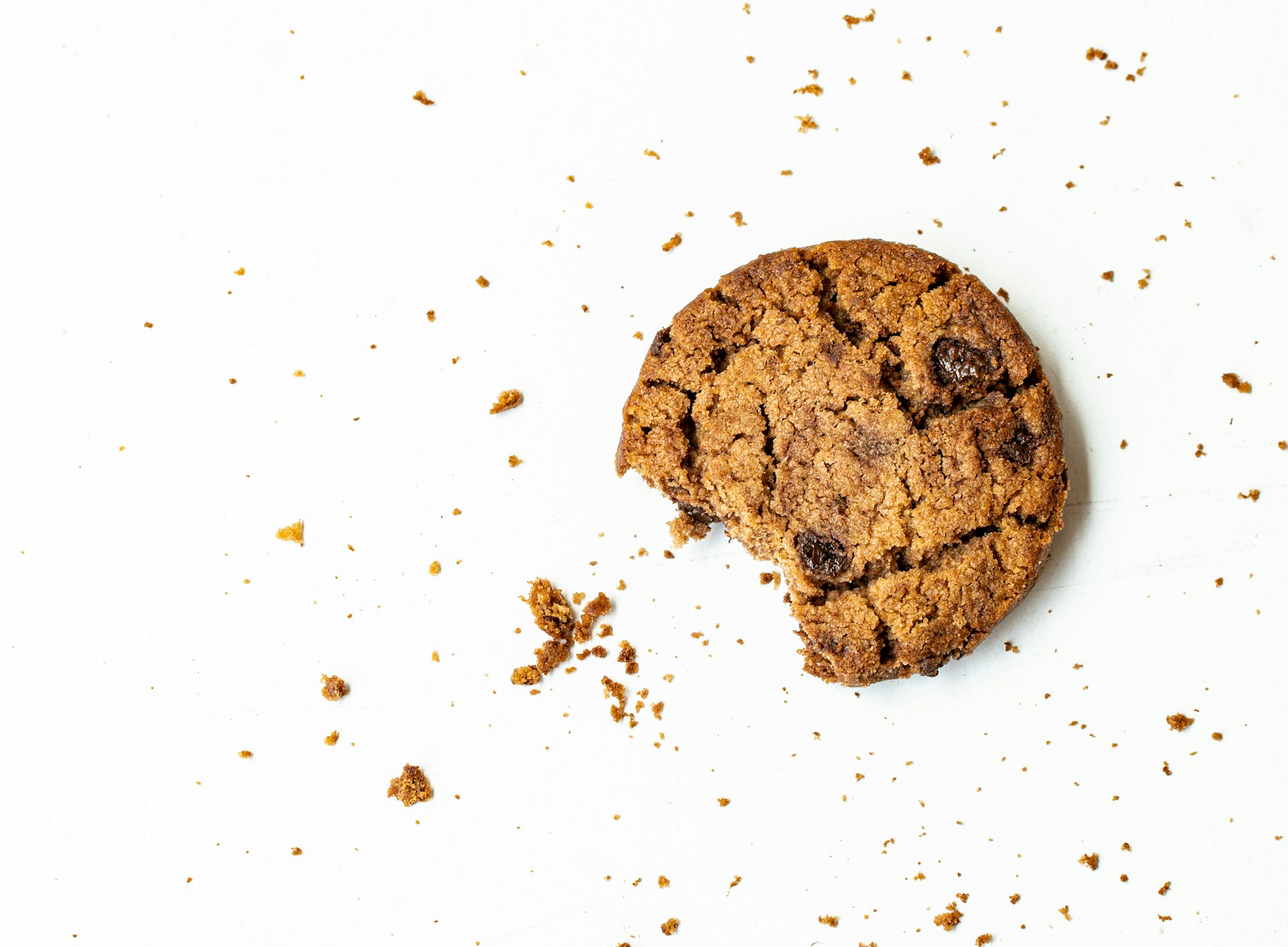 Man sieht einen angebissenen Cookie mit Krümeln auf einer weißen Fläche