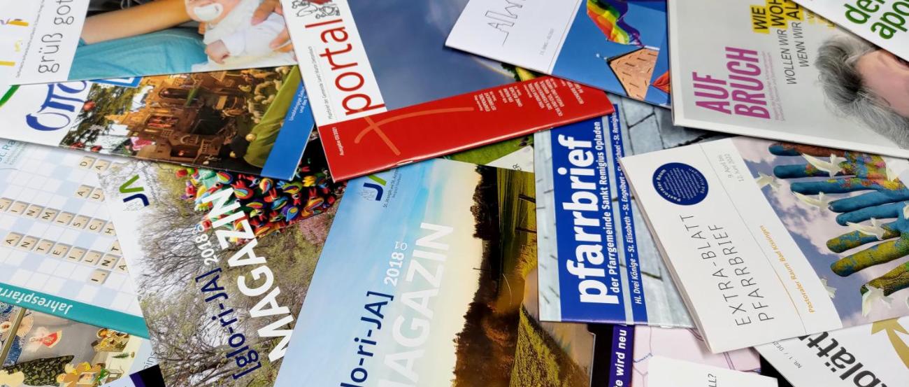 Man sieht viele bunte Pfarrebriefe durcheinander auf einem Tisch liegen
