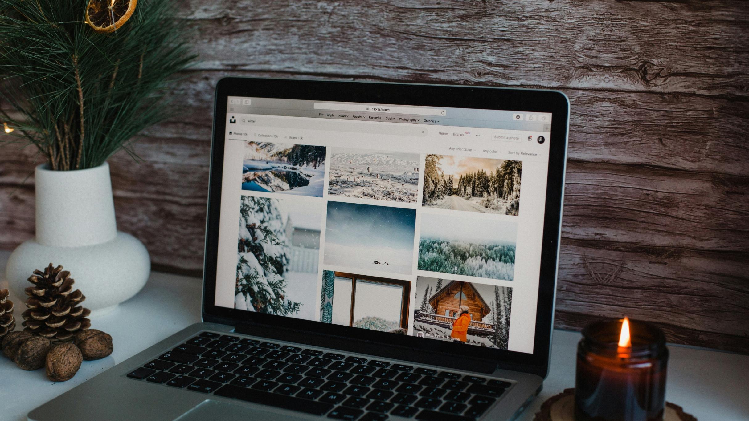 Vor einer Holzwand steht ein Laptop mit Winterbildern. Daneben auf dem Tisch ist Weihnachtsdeko zu sehen