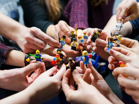 viele Hände halten unterschiedliche Minitaturfiguren zu einem Kreis zusammen