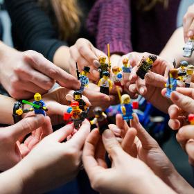 viele Hände halten unterschiedliche Minitaturfiguren zu einem Kreis zusammen