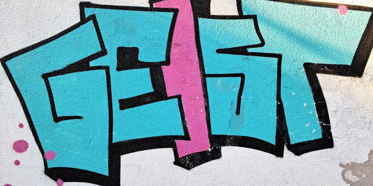 Buntes Graffiti mit dem Wort 'GEIST' in Blau und Rosa auf einer weißen Wand.