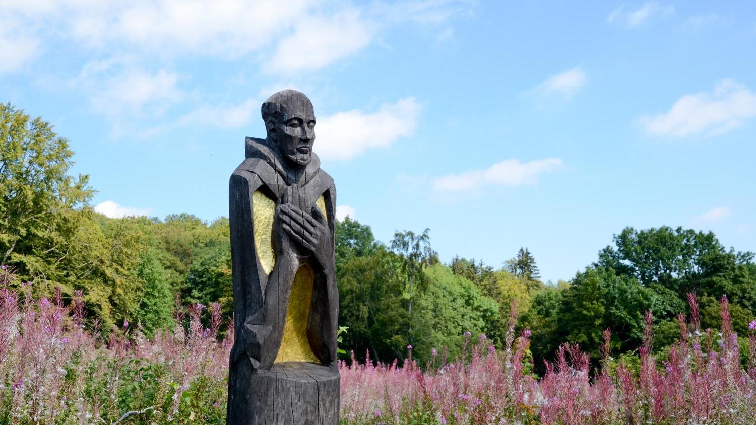 Holzskulptur im Park, umgeben von blühenden rosa Blumen und grünem Laub.