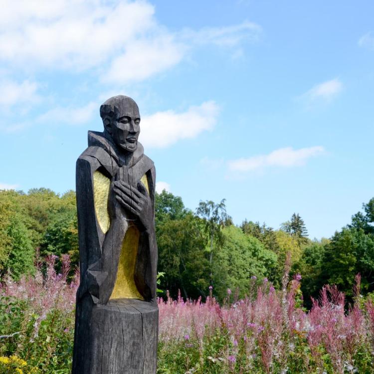 Holzskulptur im Park, umgeben von blühenden rosa Blumen und grünem Laub.