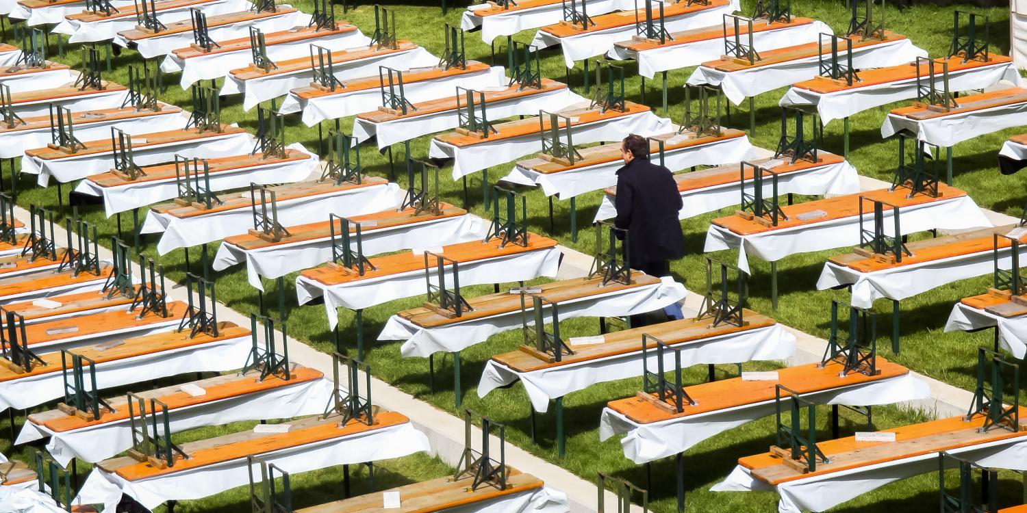 Viele leere Bierbänke und -tische stehen auf einer Wiese, eine Person geht dazwischen.