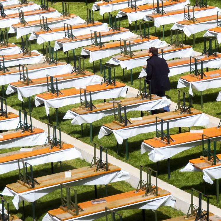 Viele leere Bierbänke und -tische stehen auf einer Wiese, eine Person geht dazwischen.