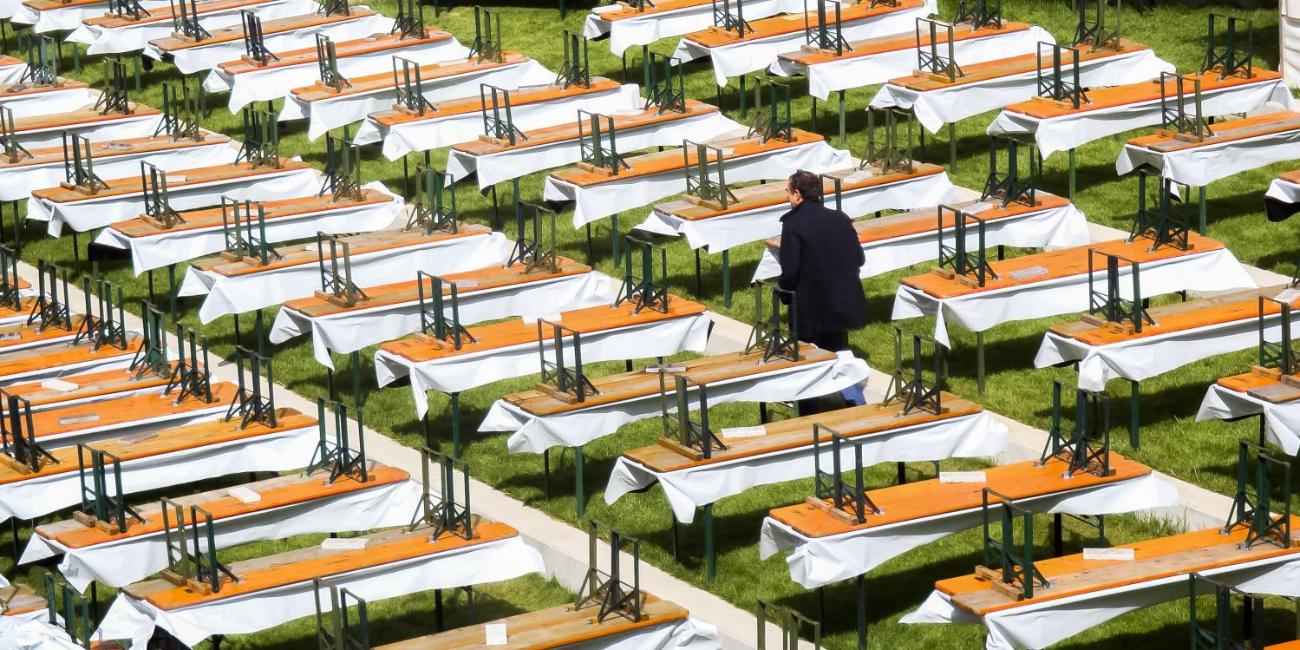 Viele leere Bierbänke und -tische stehen auf einer Wiese, eine Person geht dazwischen.