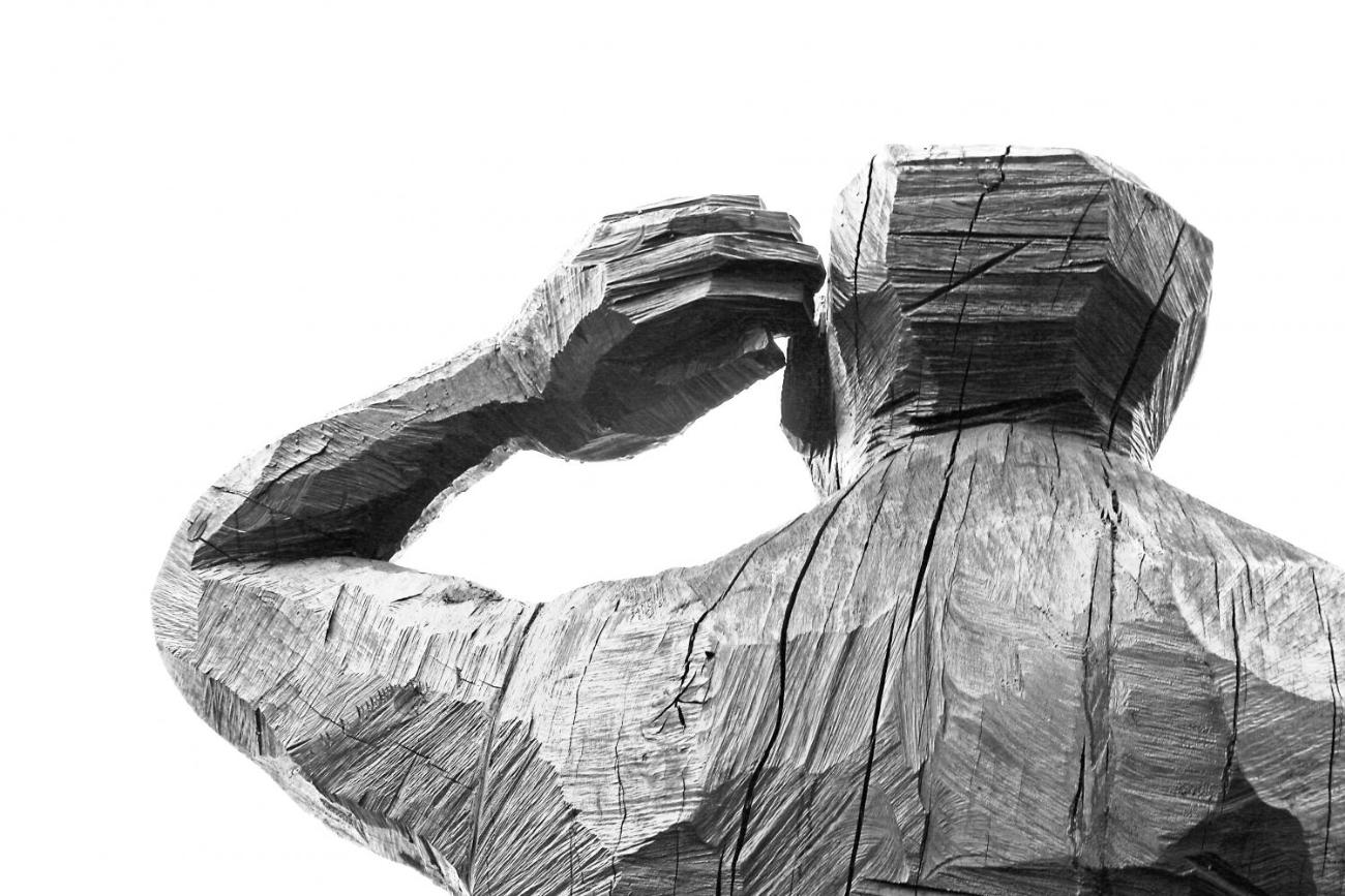 Die Holzfigur eines Menschen der sich die Hand ans Ohr legt.