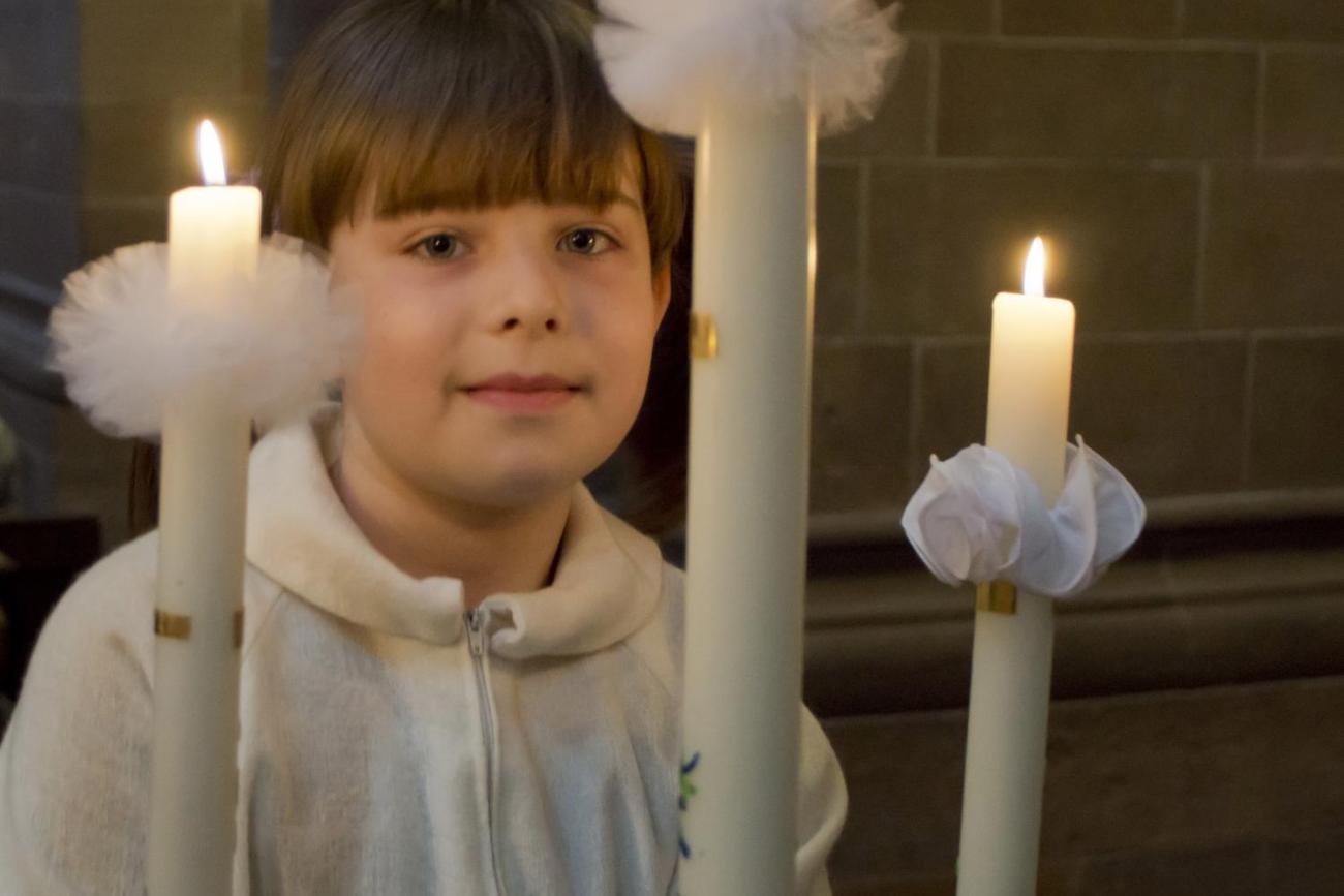 Ein Mädchen hält eine brennende Kerze.
