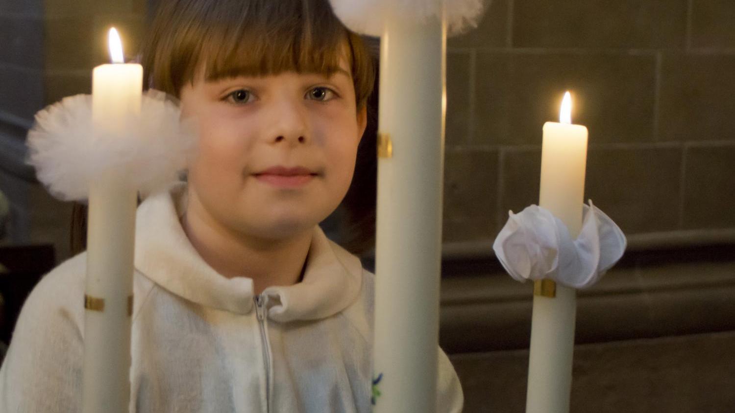 Ein Mädchen hält eine brennende Kerze.