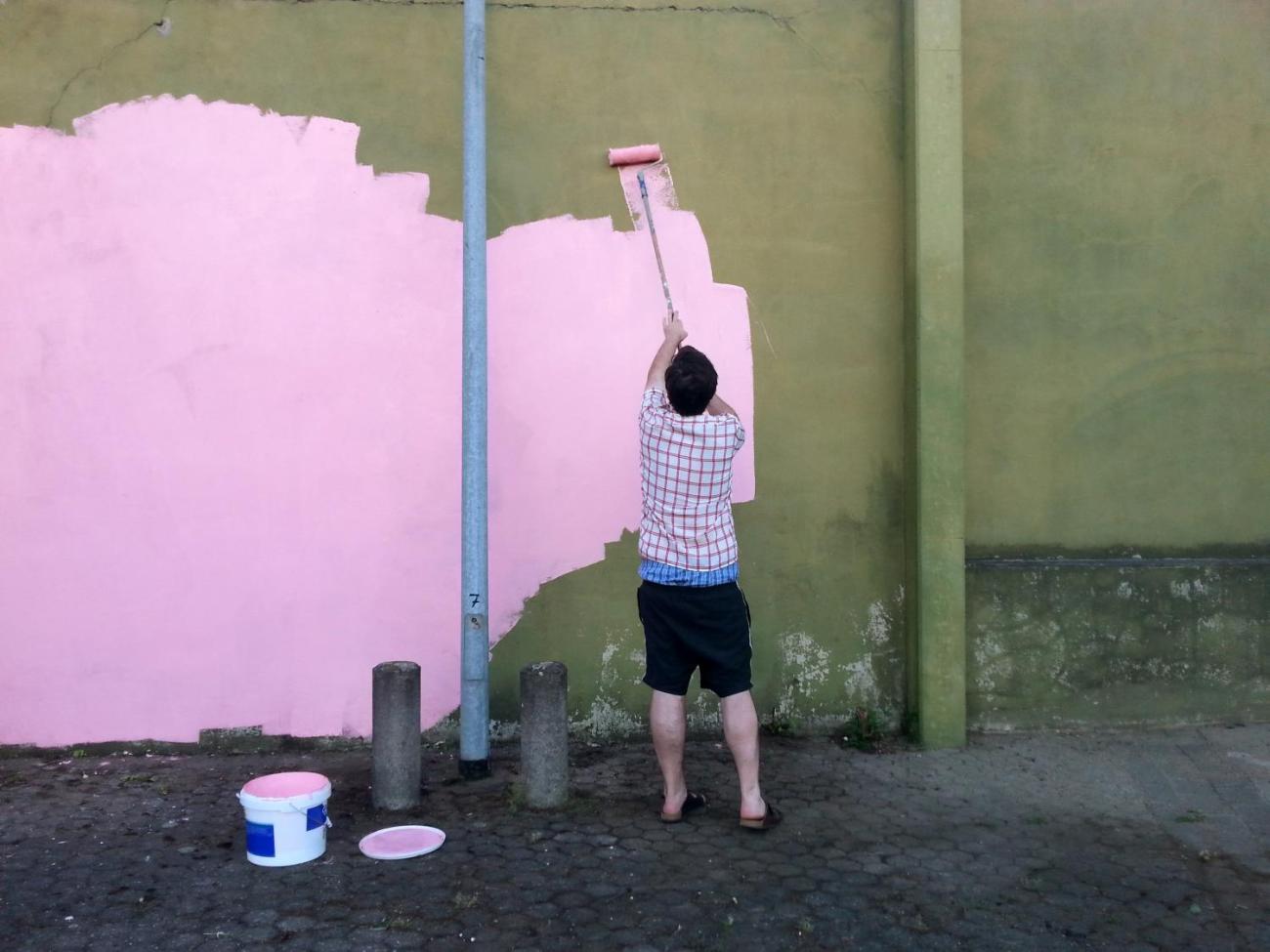 Ein Mann streicht eine graue Wand mit rosa Farbe an.